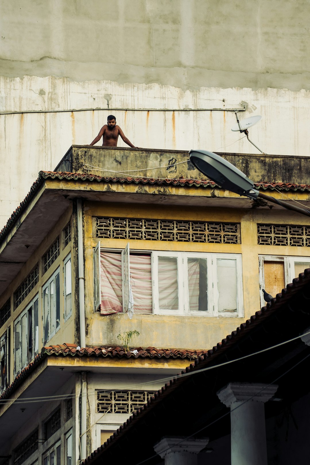d7028188a2804df08abd13bf043c20fd A shirtless man leaning on the edge of a yellow building rooftop
