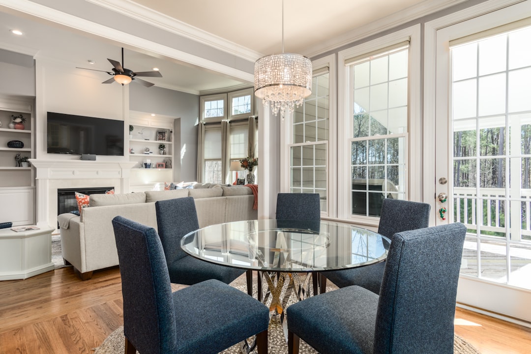 db4e6857faa24929ad75965564460ce2 A glass dining table with four blue chairs in a sunlit open living room