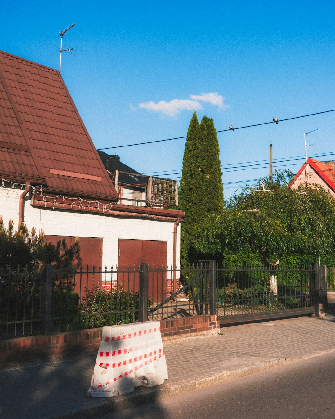 White house with brown roof, fence, and barrier on sidewalk