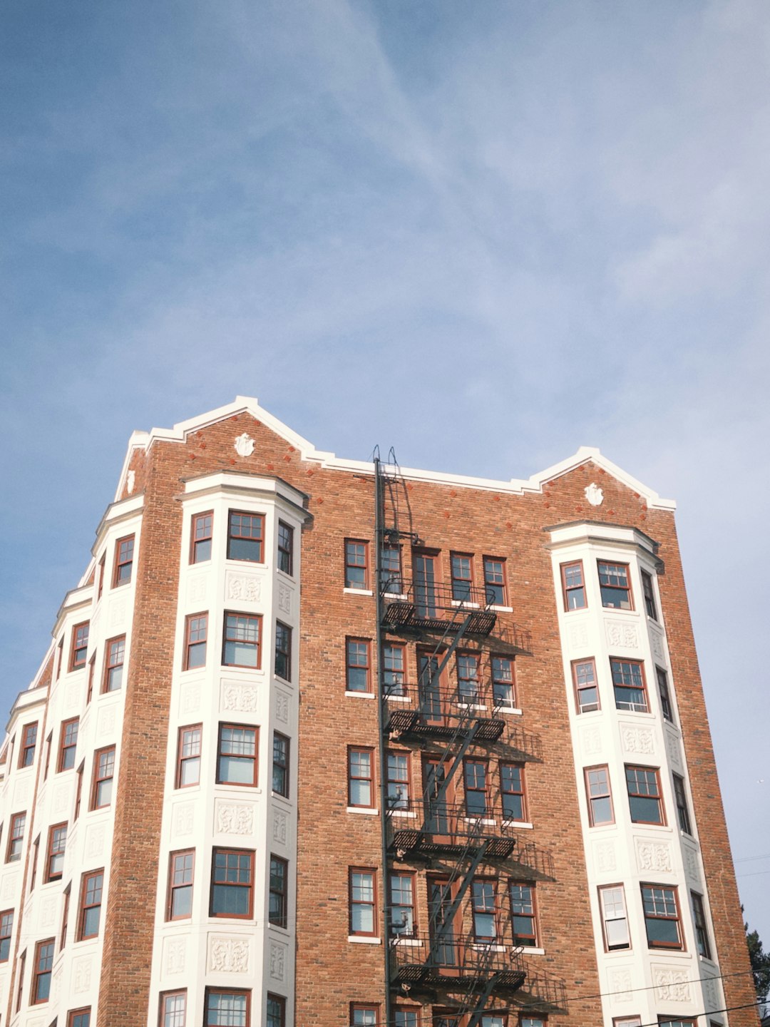 e3bb0000742c44478bfc8267a9663d9a A red brick apartment building with white bay windows and a black fire escape