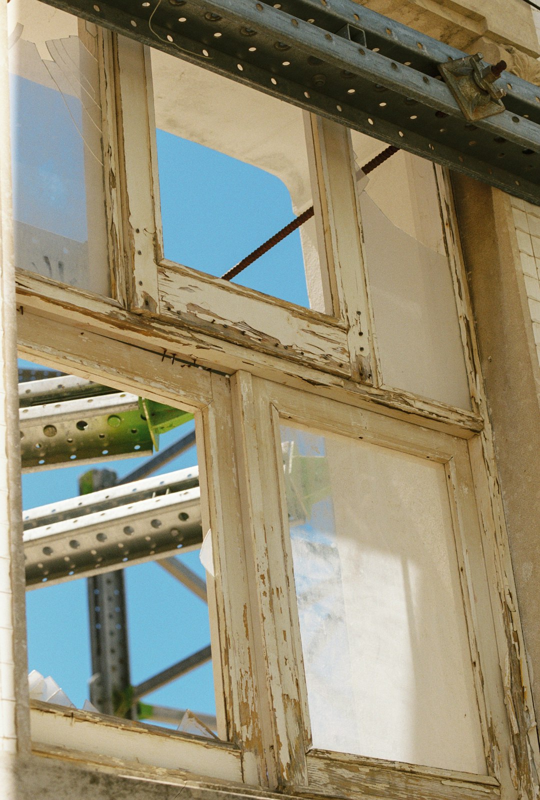 Peeling paint on a wooden window frame with exposed steel scaffolding against blue sky