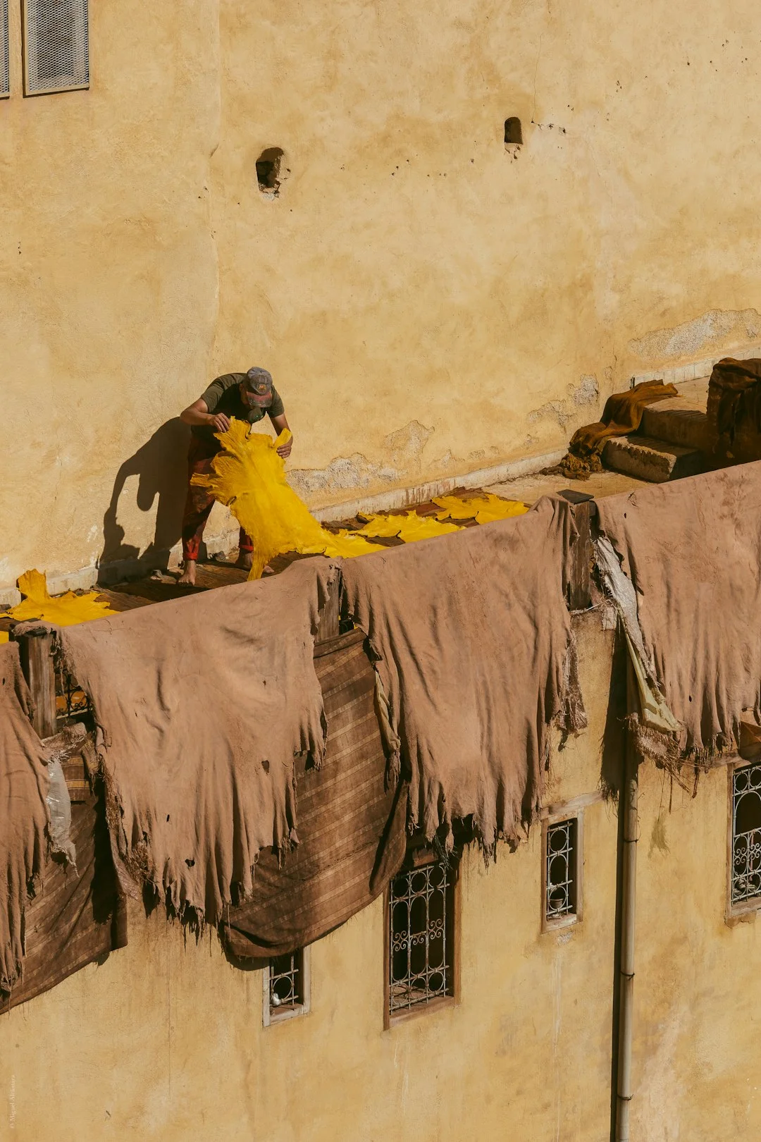 Roofing Work on Stucco Building Man applying roofing material on a flat rooftop of a pale yellow stucco building