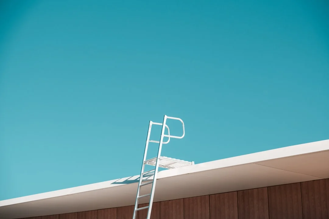 Metal ladder leaning against a flat roof with a safety rail platform above