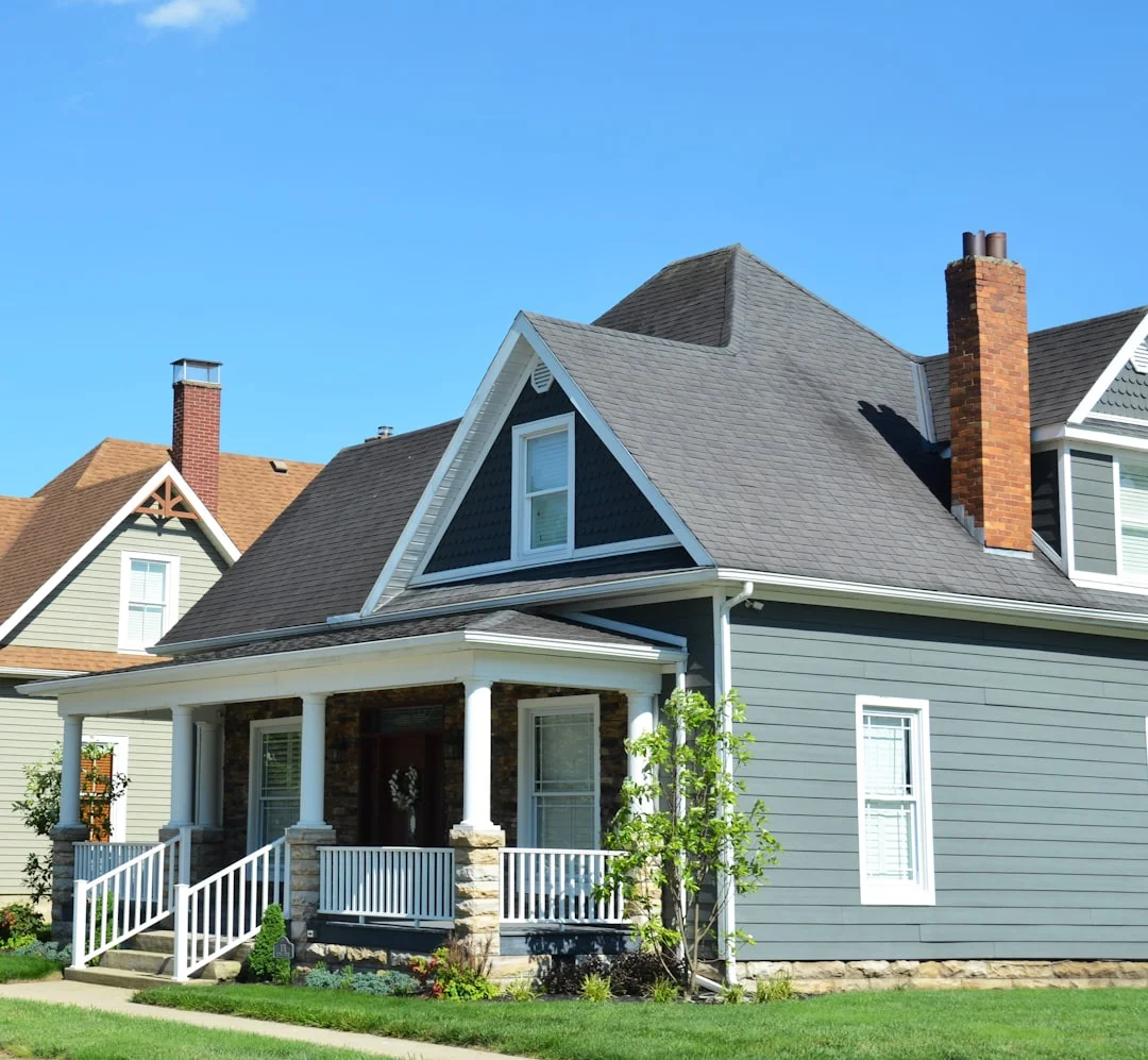 Two-Story House with Shingled Roof A blue house with a white porch and red chimney.