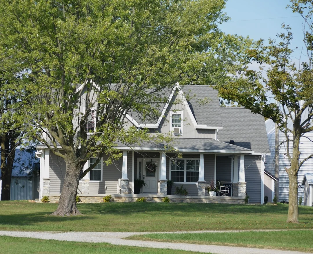 Single-Family House with Porch A grey house with a porch and trees.