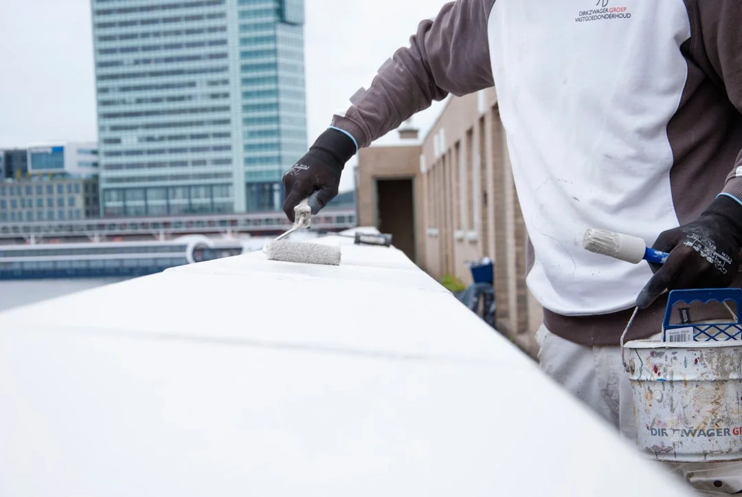 Rooftop Coating Application Person painting the edge of a rooftop with a roller and brush